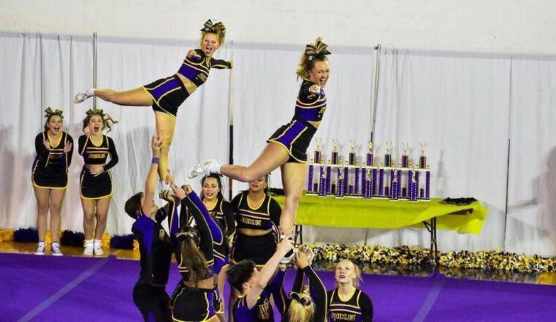 Two female cheerleaders hold leg extensions as they are lifted up high